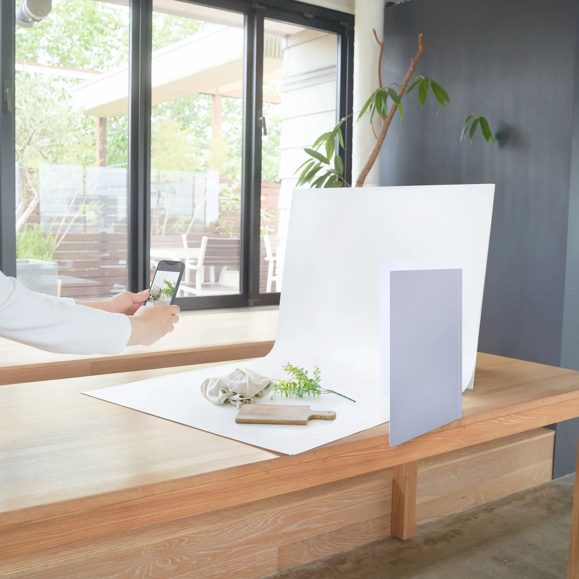 自然光の入る部屋で白い背景シートを使いスマホで小物を撮影するシーン