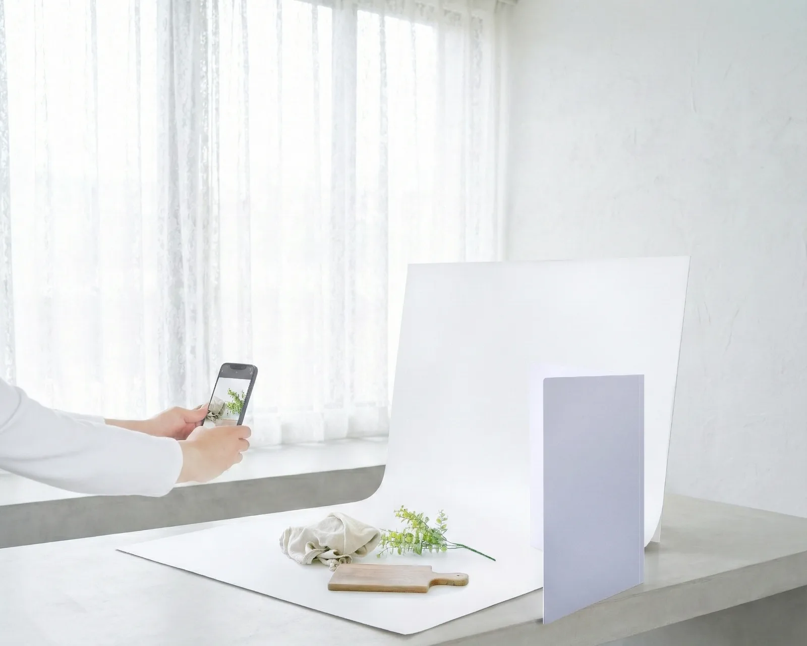 明るい部屋で背景シートを使い、スマホで小物を撮影するシーン